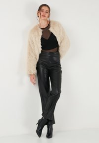 Crème nepbontjacket over een zwarte doorschijnende top, gecombineerd met zwarte high-waisted neplederen broek en enkellaarsjes met een spitse neus.