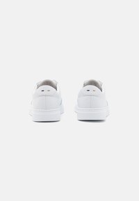 White leather sneakers with a smooth texture, featuring a rounded toe, flat sole, and subtle black and gold accents at the heel.