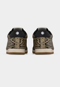 Paire de baskets basses avec motif peau de serpent marron et noir, languette de talon noire et semelles blanches, vues de dos sur un fond blanc.