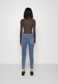 Hnědý top s dlouhým rukávem a modré džíny s vysokým pasem a rovnými nohavicemi, viděné zezadu. Černé boty s masivní podrážkou.