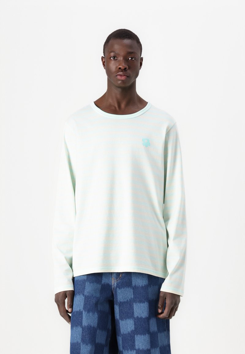 Long-sleeve shirt in light mint with horizontal stripes, featuring a small blue graphic and a round neckline. Paired with patterned blue pants.