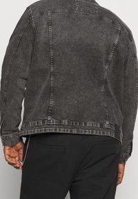 Vista posteriore di una persona che indossa una giacca di jeans nera sbiadita e pantaloni neri, con una catena d'argento appesa dalla tasca.