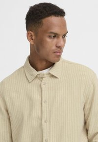 Beige, ribbet stofskjorte med knaplukning foran, spids krave og subtil tekstur. Har beige knapper og en afslappet pasform.