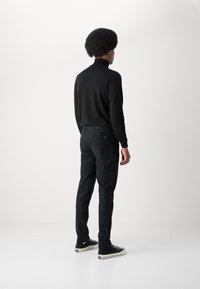 Pull à col montant noir associé à un pantalon sombre et des baskets en toile noires. Le tissu semble lisse avec un design ajusté.