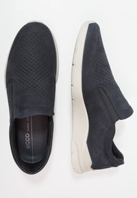 Tengeri slip-on cipők perforált felsőrésszel, kontrasztos világosszürke talppal, puha velúr textúrával és elasztikus oldalsó kiegészítőkkel a megfelelő illeszkedésért.