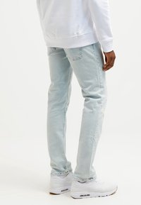 Person wearing light blue slim-fit jeans, white sneakers, and a white sweatshirt, standing against a plain background.