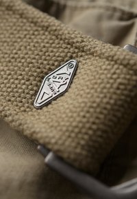 Ceinture en tissu tissé beige avec une étiquette en métal argenté. Elle dispose d'une boucle rectangulaire et d'un matériau texturé. La vue rapprochée met en évidence les détails.