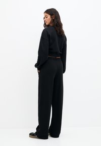 Sweatshirt noir court et pantalon de survêtement noir ample, en tissu doux avec une taille élastique, vus de derrière.