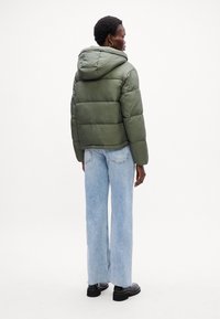 Pufferjakke i olivengrønn, med hette, quiltet tekstur og cropped design. Kombinert med lyseblå vide bukser og svarte støvler.