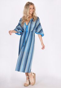 Hosszú, mintás kék kimono, derékmegkötővel, kék különböző árnyalataiban hullámmintával és mély V-nyakkal. Strasszos szandálra viselve.