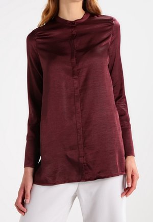 Camicia a maniche lunghe bordeaux con design a bottoni, lucentezza sottile e colletto alto. Il tessuto appare liscio con un leggero drappeggio sulle spalle.