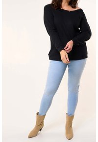 Pull noir à côtes avec un design décolleté, associé à un jean skinny bleu clair et des bottines à talons hauts beiges.