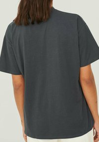 T-shirt in cotone grigio scuro, con una vestibilità ampia, maniche corte e parte posteriore lisa. Presenta una texture morbida e un collo rotondo.