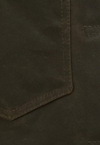 Σκούρο καφέ ύφασμα με λεία υφή, διαθέτοντας μια καπιτονέ τσέπη και αντίθετη ραφή. Το υλικό φαίνεται ανθεκτικό και στιβαρό.