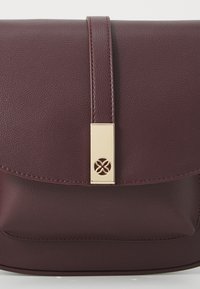 Sac à main en cuir bordeaux de forme rectangulaire, texture lisse, avec un fermoir doré présentant un détail découpé en forme de fleur.