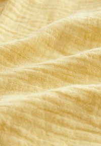Tessuto giallo chiaro con un aspetto testurizzato e spiegazzato. Materiale morbido e leggero con una leggera lucentezza e un motivo tessuto.