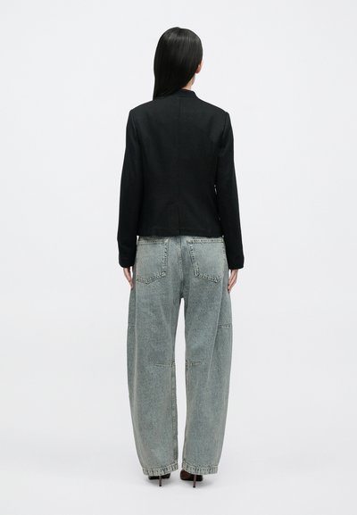 Sort cropped jakke med lange ærmer, parret med oversized lyseblå denimjeans med falmet tekstur og synlige syningsdetaljer.