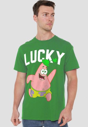 Grünes Baumwoll-T-Shirt mit einer Cartoonfigur, Patrick, und dem Wort "GLÜCKLICH" in weißen, fettgedruckten Buchstaben über einem Akzent aus einem vierblättrigen Kleeblatt.