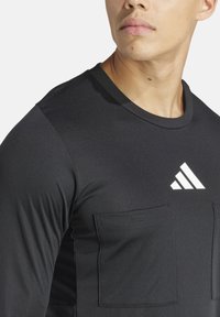 Zwarte langmouwen sportshirt gemaakt van gladde, rekbare stof. Beschikt over twee voorkoffers en een wit Adidas-logo op de borst.