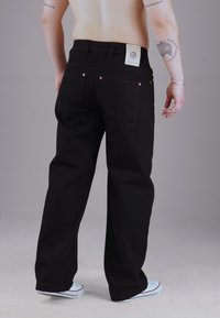 Schwarze Denim-Jeans mit geradem Bein, ausgestattet mit einem Leder-Patch-Label, Kupfer-Nieten und einem nahtlosen Rücktaschendesign.