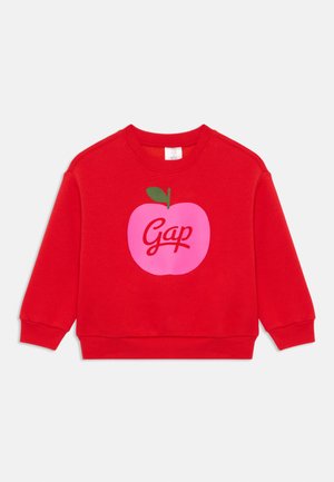 Sweatshirt rouge en coton, avec un grand graphique de pomme rose accompagnée d'une feuille verte et du mot "Gap" en lettres cursives blanches.