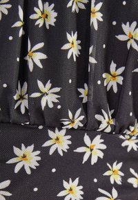 Svart tyg med blommönster som har vita och gula tusenskönor samt små vita prickar. Tyget har en strukturerad yta och plisserad design.