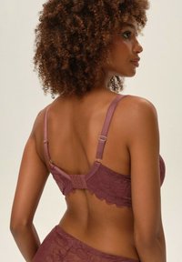 Koronkowy biustonosz w kolorze mauve z regulowanymi ramiączkami, zapięciem na haftki oraz kwiatowym wzorem wykończenia. Miękka, teksturowana tkanina.