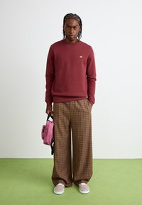 Burgunderfarget hettegenser, rutete vide bukser i brun og blå, grå sneakers og en rosa veske. Jevn tekstur med uformell design.