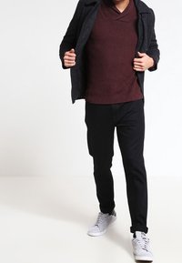 Pull côtelé bordeaux à col en V, pantalon noir, veste gris, et baskets blanches. Présente une coupe décontractée avec un design en maille texturée.