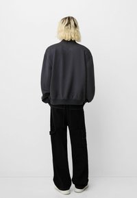 Black oversized sweatshirt with a smooth texture and ribbed cuffs, paired with wide black cargo pants featuring utility pockets.