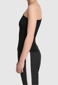 Haut sans manches noir à coupe ajustée, fabriqué en tissu doux. Le vêtement présente un design simple sans embellissements ni motifs.