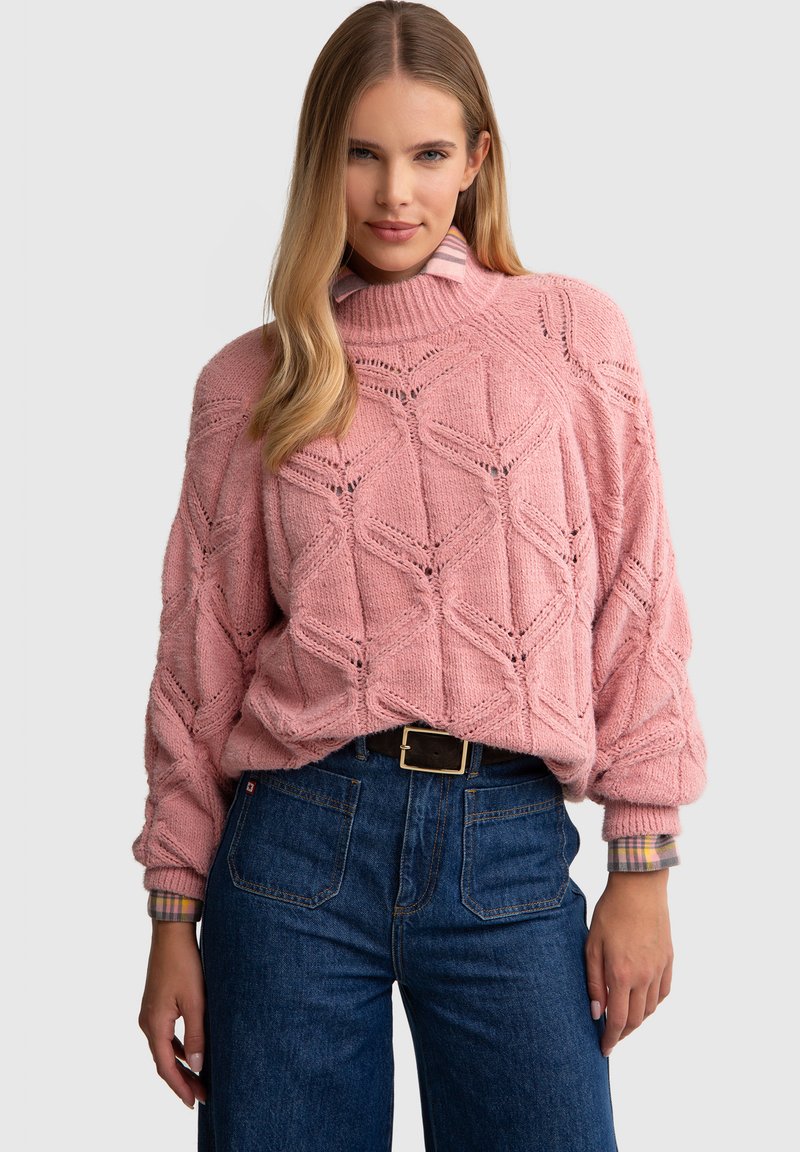 Roosa kudumine sviiter, millel on geomeetriline muster ja ribakrae; paaritatud kõrge vöökohaga tumedate teksadega, millel on ees taskud.