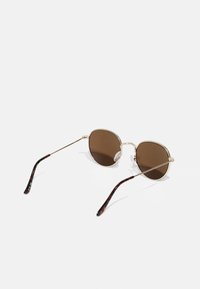 Lunettes de soleil en métal doré avec des verres marron et des fines montures en fil. Branches à motif écaille de tortue avec des patins de nez pour le confort.