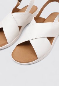 Sandalias de cuero blanco con correas entrecruzadas y una plantilla en tono bronceado. Diseñadas con un diseño de punta abierta y una suela flexible para mayor comodidad.