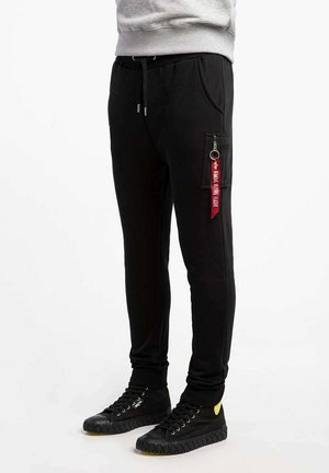 Schwarze Sweatpants mit verstellbarem Bund, Seitentaschen und einer Reißverschlusstasche mit einem roten Schlüsselanhänger. Strukturiertes Material, lockere Passform.