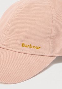 Κασκόλ από κοτλέ σε απαλό ροζ με καμπυλωτή γείσο. Διαθέτει κίτρινη κεντημένη λογότυπο "Barbour" μπροστά. Επιφάνεια με υφή και ραφές λεπτομερειών.