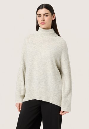 Gaišpelēks, pārmērīgi liels turtlenecks džemperis ar mīkstu tekstūru, ribotām aprocēm un apakšmalu, kuram ir brīva siluets un sānu šķēlumi.
