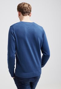 Niebieski sweter z miękkiego materiału z okrągłym dekoltem oraz ściągaczami na rękawach i dole. Charakteryzuje się gładką fakturą i subtelnym wycięciem w serek z tyłu.