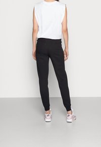 Bílý bezrukávový top, černé joggers a světle růžové sportovní boty. Joggers mají přiléhavý design s elastickými manžetami na kotnících.