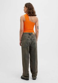 Top corto de canalé naranja con un tirante, combinado con unos vaqueros oscuros de tiro alto y holgados, que presentan bolsillos traseros y zapatos en tonos neutros.
