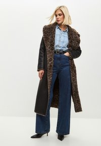 Pitkä musta takki, jossa leopardikuosinen karvareunus, pidettynä sinisen farkkupaidan ja korkeavyötäröisten sinisten farkkujen päällä. Mustat terävät korkokengät viimeistelevät asun.