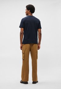 Camiseta de algodão azul-marinho, de mangas curtas, combinada com calças cargo castanhas com dois bolsos laterais e um ajuste solto, vista de trás.