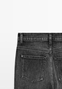 Back view of dark gray denim jeans showing two back pockets and belt loops on a white background.