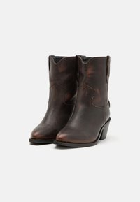 Bottes de cowboy en cuir brun avec un bout pointu, des détails cousus et un talon empilé. Présente des coutures latérales surélevées et une finition texturée.