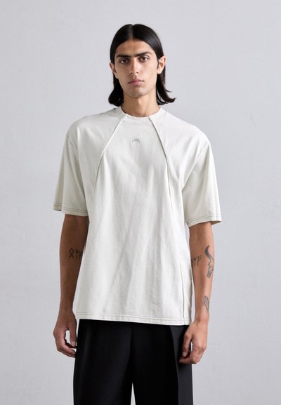 Jasno beżowy, oversize'owy t-shirt wykonany z bawełny. Posiada krótki rękaw, prążkowany dekolt oraz subtelny detal z logo z przodu.
