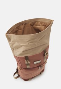 Roll-top backpack in brown and beige. Made of durable fabric with adjustable straps, featuring a front pocket and buckle closures.