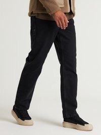 Pantalones de mezclilla negros con un corte recto, contrastados por una chaqueta beige. La tela tiene una textura suave y detalles de hardware mínimos.
