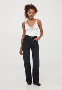 Jeans neri a gamba larga con vita alta, abbinati a un body bianco con rifiniture in pizzo e spalline sottili. Texture liscia, vestibilità casual.