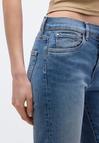 Jeansy denimowe w jasnoniebieskim kolorze z efektem przetarcia, posiadające pięć kieszeni i kontrastowe przeszycia. Prosty krój i średni stan w pasie.
