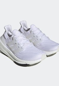 Paire de chaussures de course blanches Adidas avec tige en maille et cage à lacets translucide sur un fond clair.